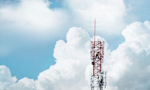 A 5G transmission tower in front of a blue sky and large white clouds