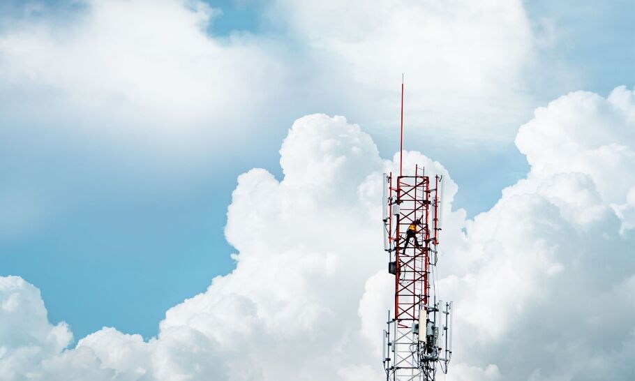 A 5G transmission tower in front of a blue sky and large white clouds